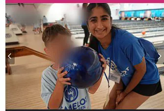 Aanya helping a child hold a bowling ball at a Camelot outing